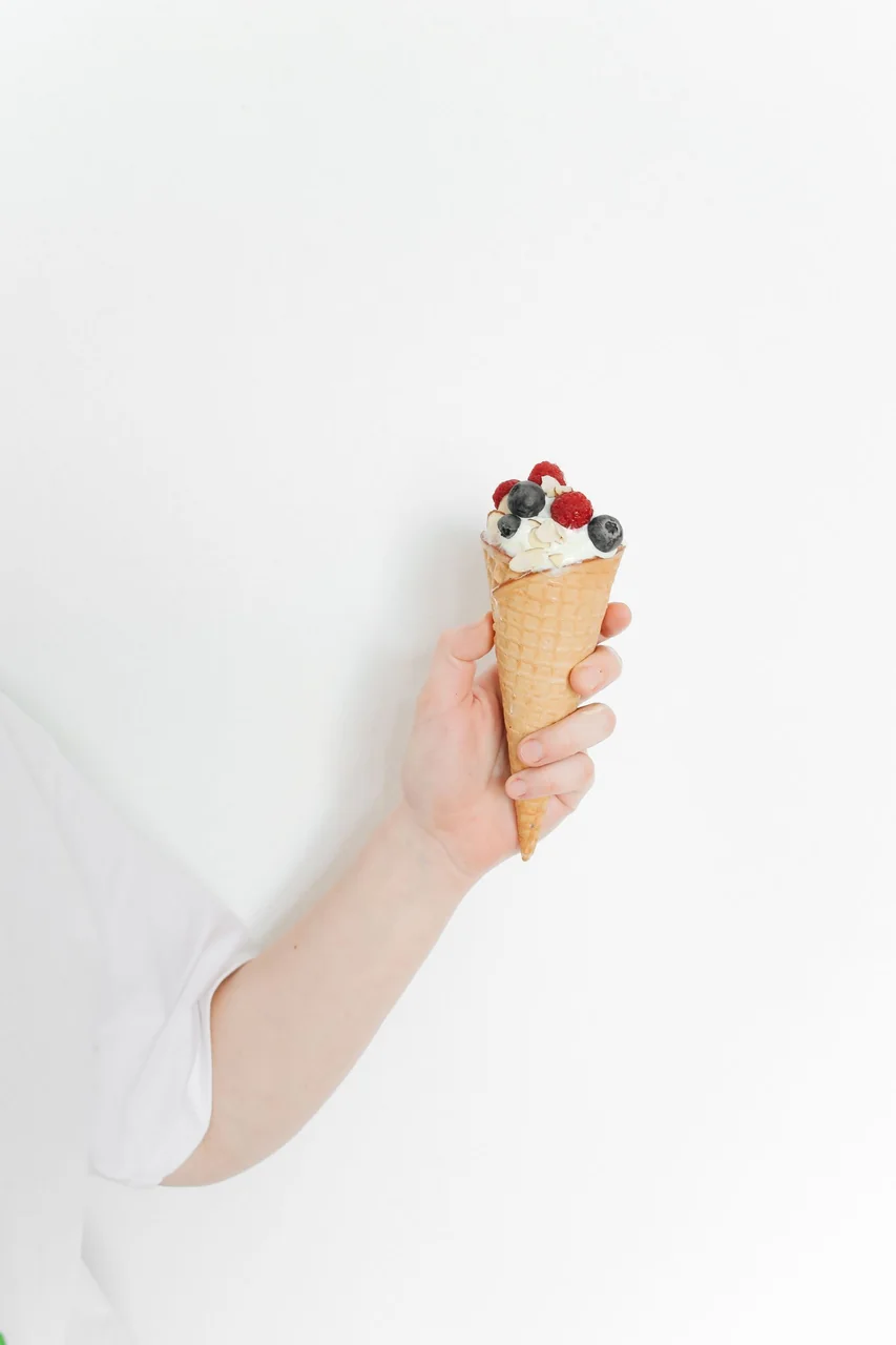 Hand holding freshly baked artisan waffle cone with ice cream and fresh raspberries